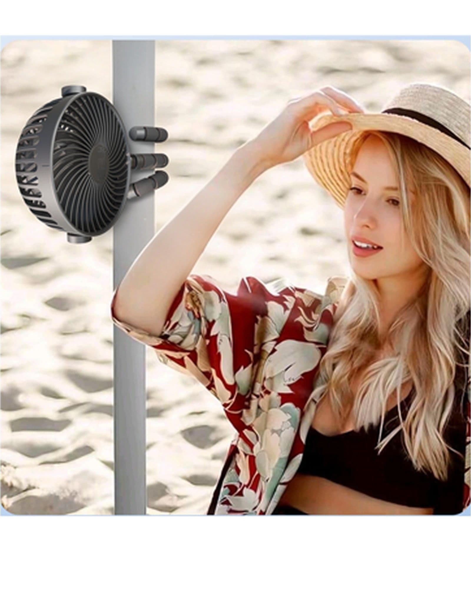 A woman in a sun hat and floral shirt sits on a beach next to an Airbro FFX-50 portable fan attached to a pole.
