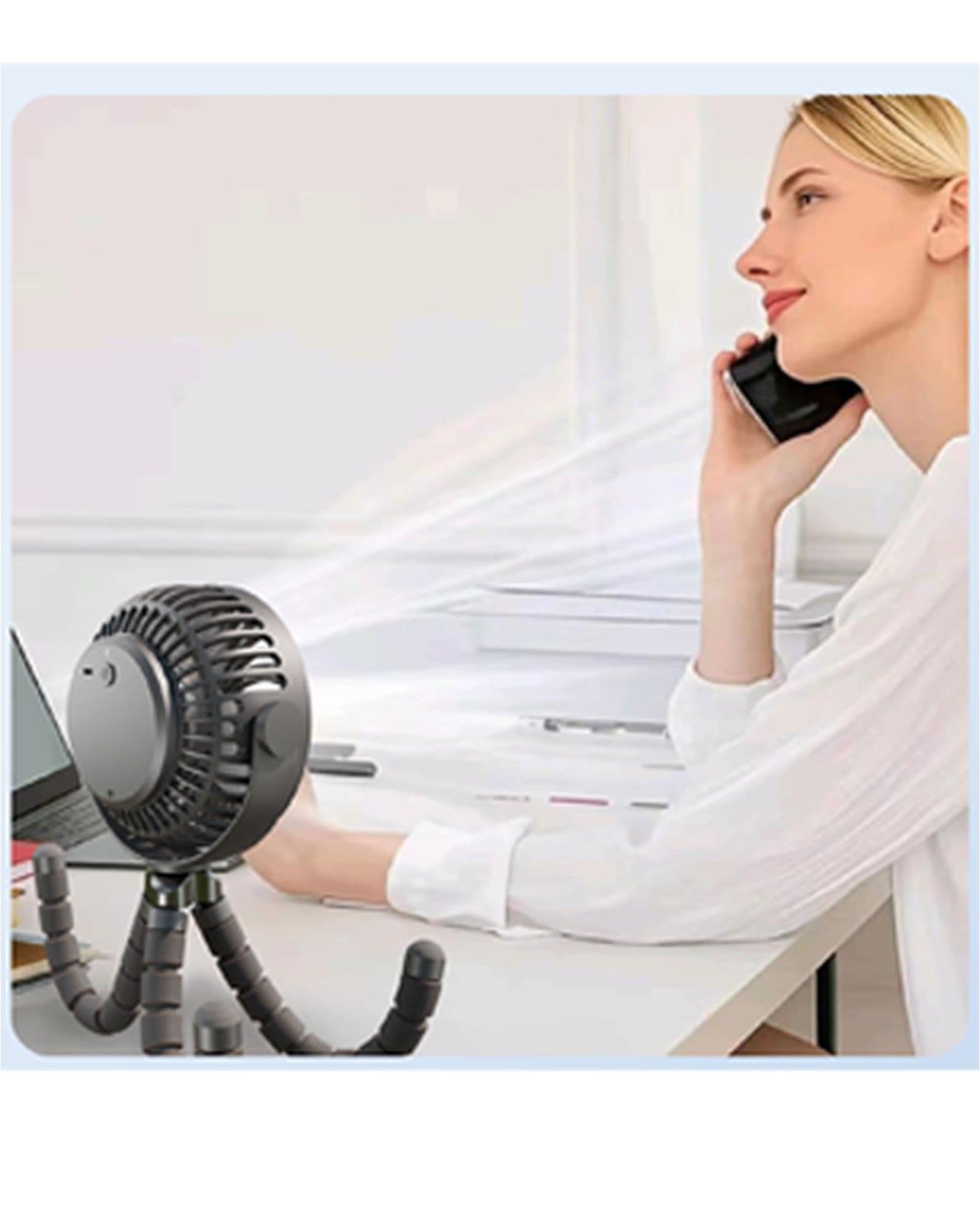 A woman sitting at a desk talking on a phone while an Airbro FFX-50 portable tripod fan blows air toward her.