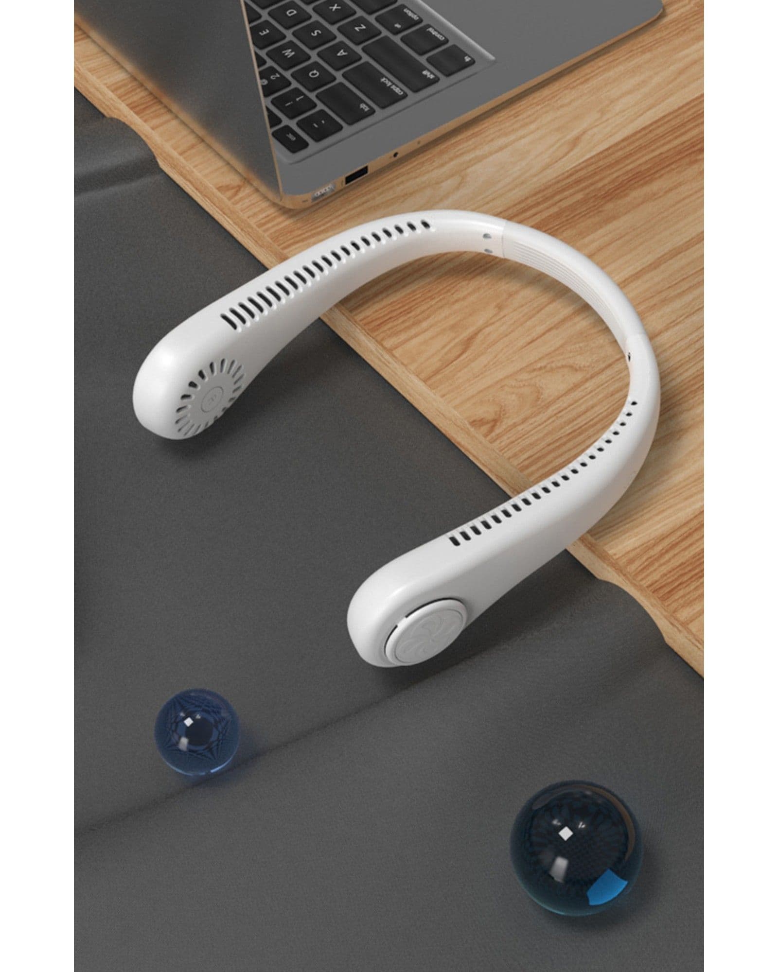 Airbro FNE-100 white wearable neck fan resting on a desk next to a laptop.