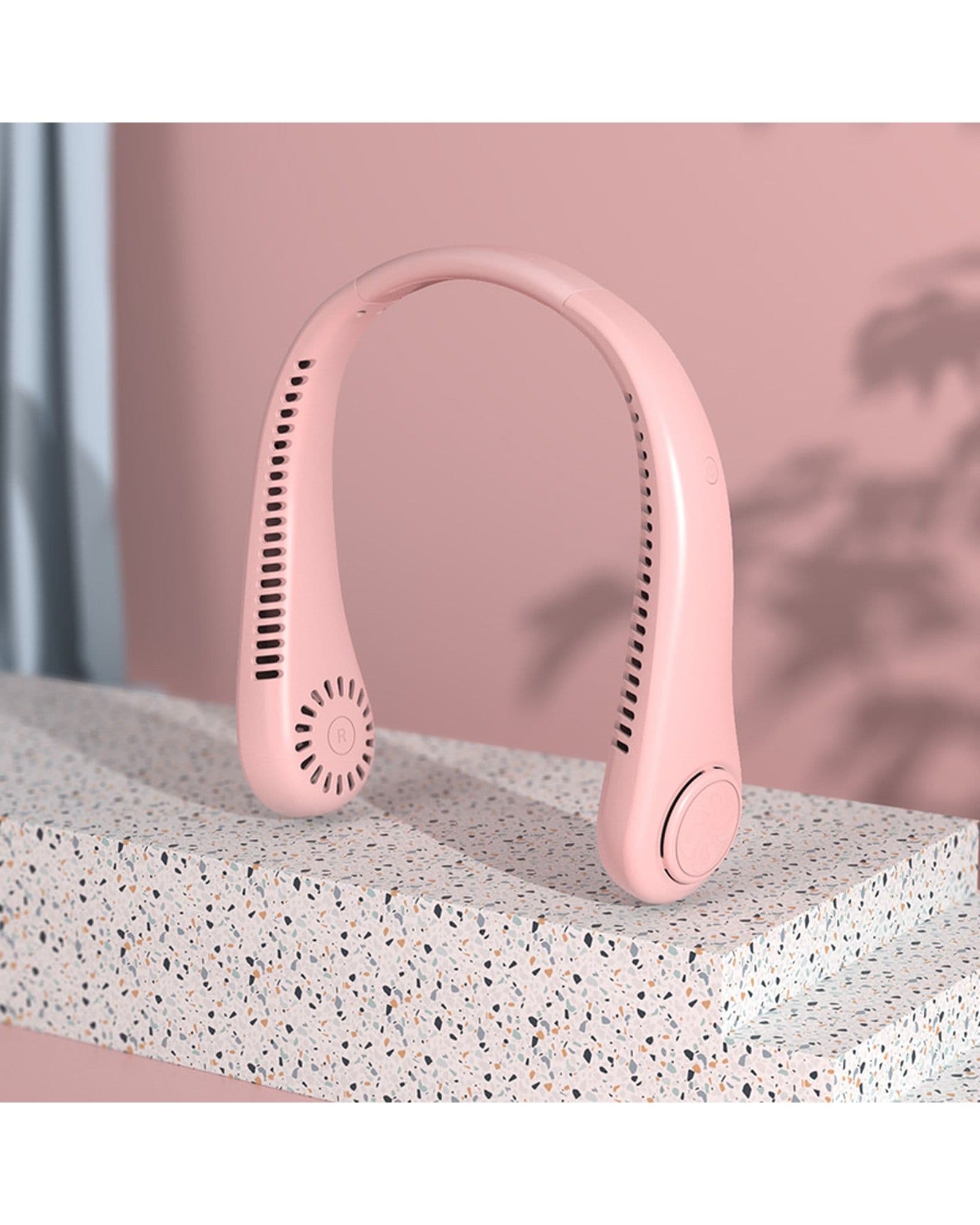 A pink Airbro FNE-100 wearable neck fan resting on a speckled stone surface against a soft pink background.