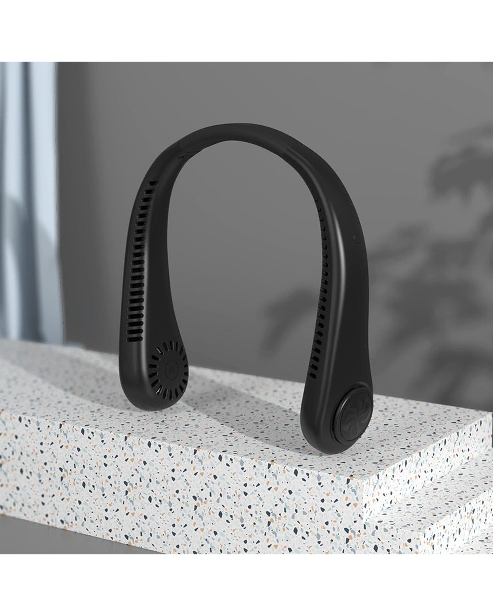 A black Airbro FNE-100 wearable neck fan resting on a speckled stone surface in a modern indoor setting.