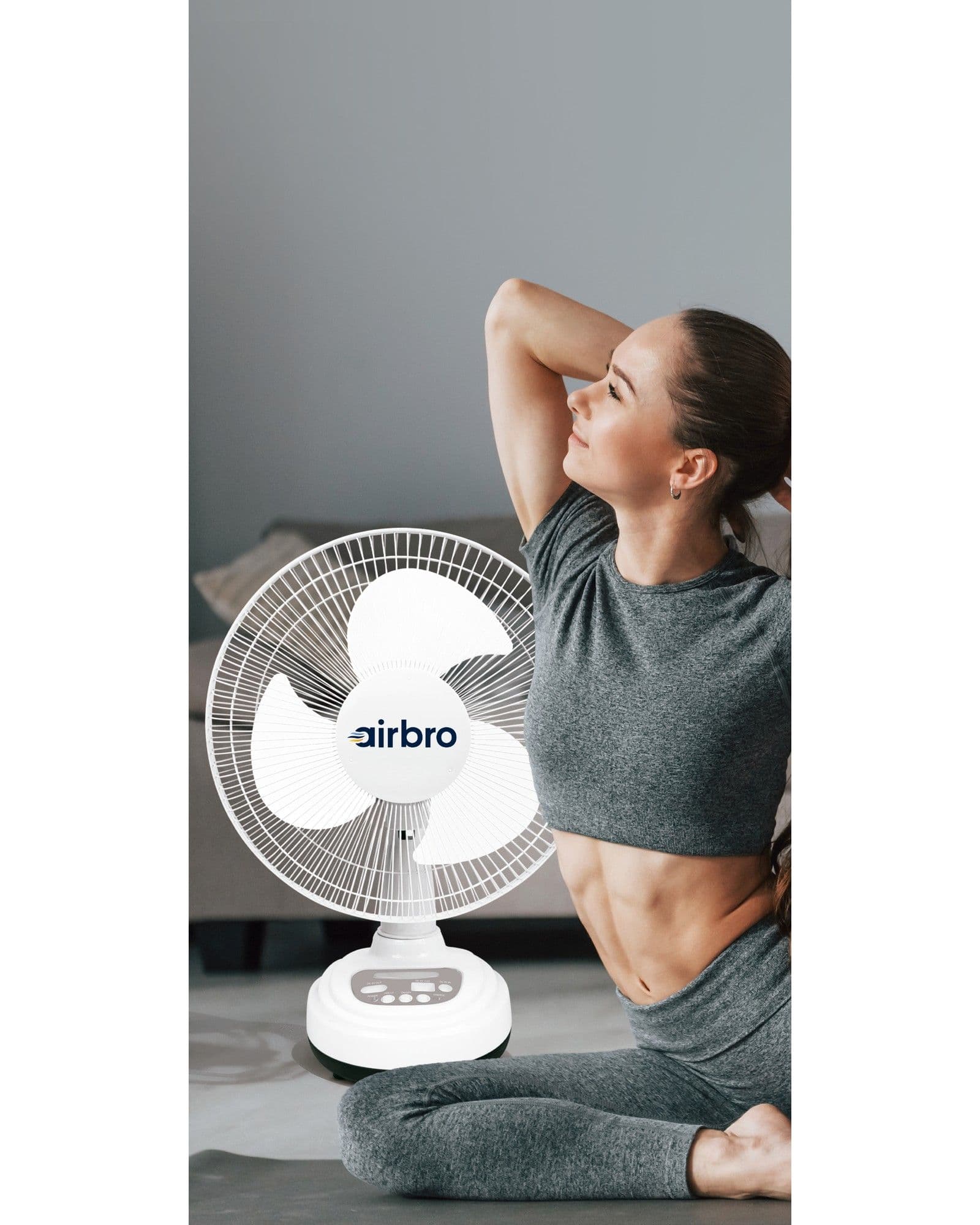 A woman in workout clothes stretching next to an Airbro FSA-12 white desk fan in a home setting.