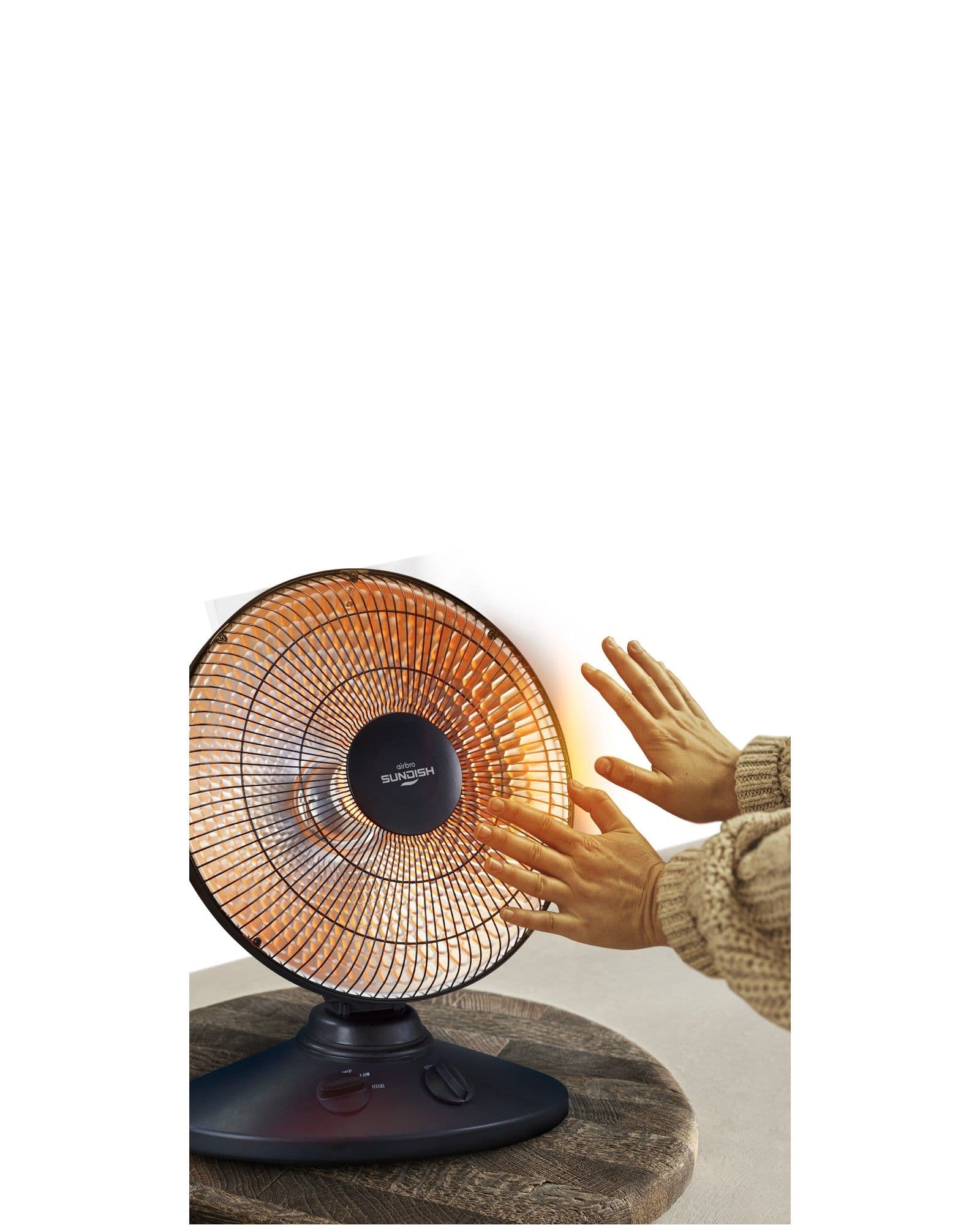 A person warming their hands in front of a glowing, circular electric heater on a wooden table.
